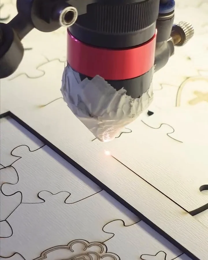 Cabeçote vermelho do laser cortando o contorno de peças em uma placa de madeira